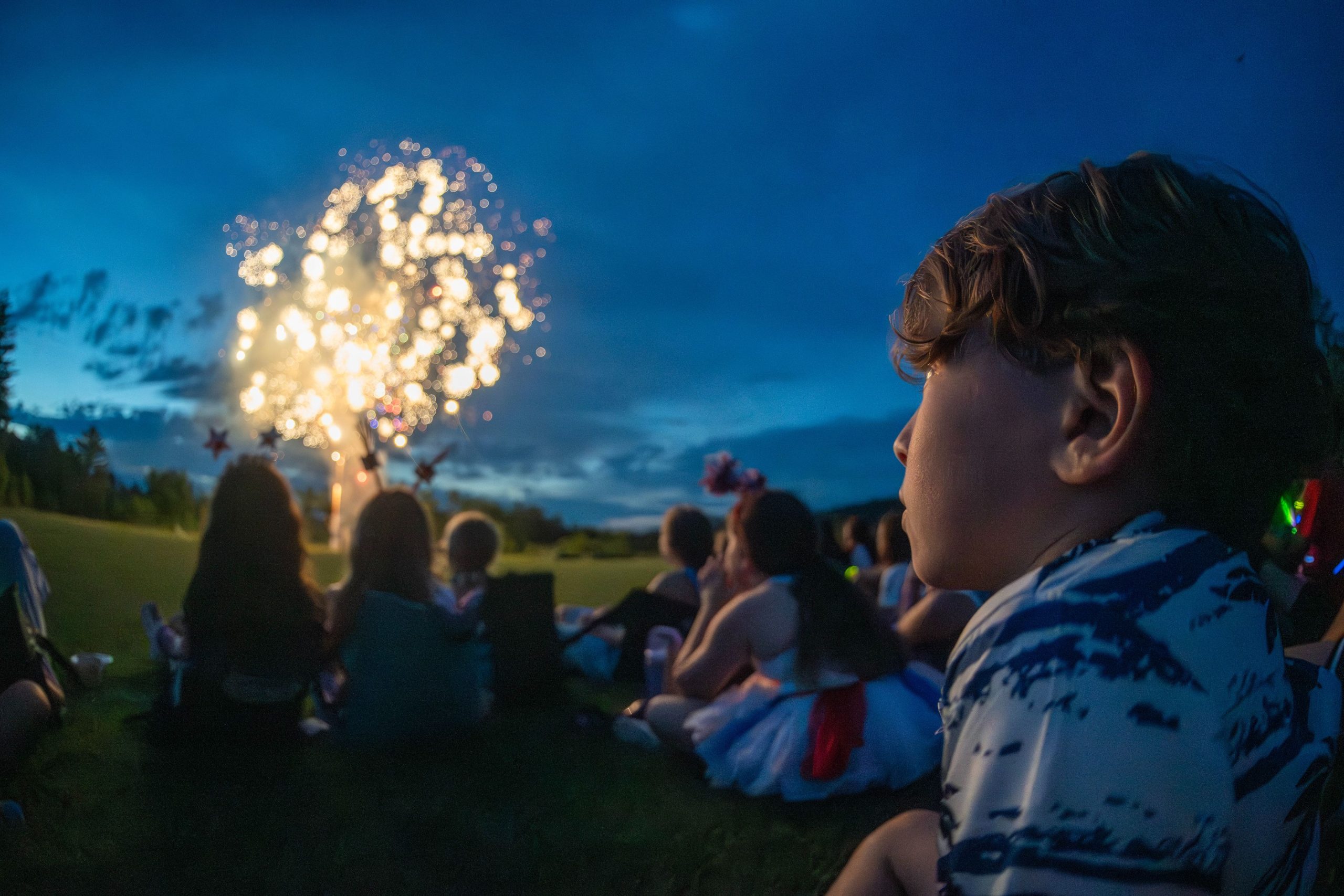 Campers on the grass watching fireworks on a summer night